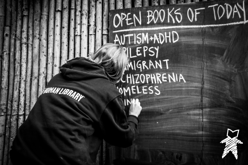 person writing book titles on a chalk board for the Human Library