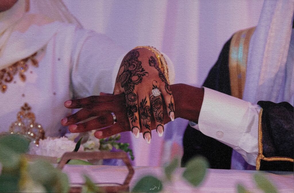 Aphoto of a woman's hand with ornate decorations on the skin and nails, on top of a graceful man's hand in a wedding ceremony