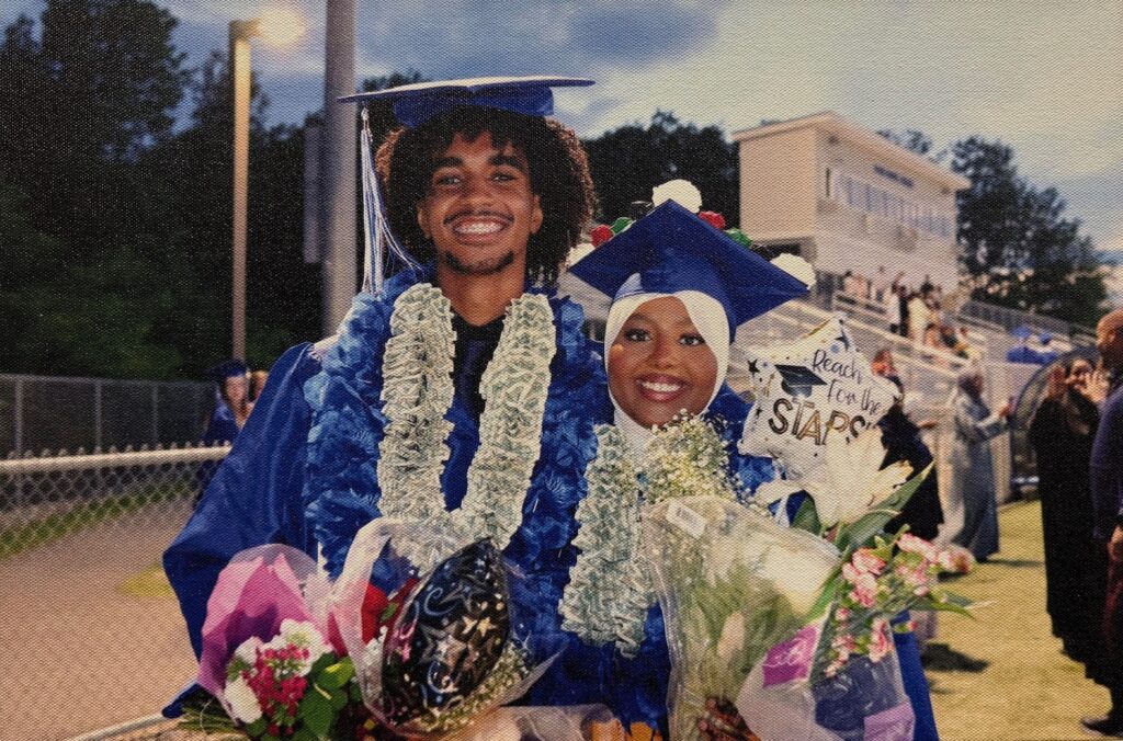 A photo of two young people wearing blue graduation robes holding flowers
