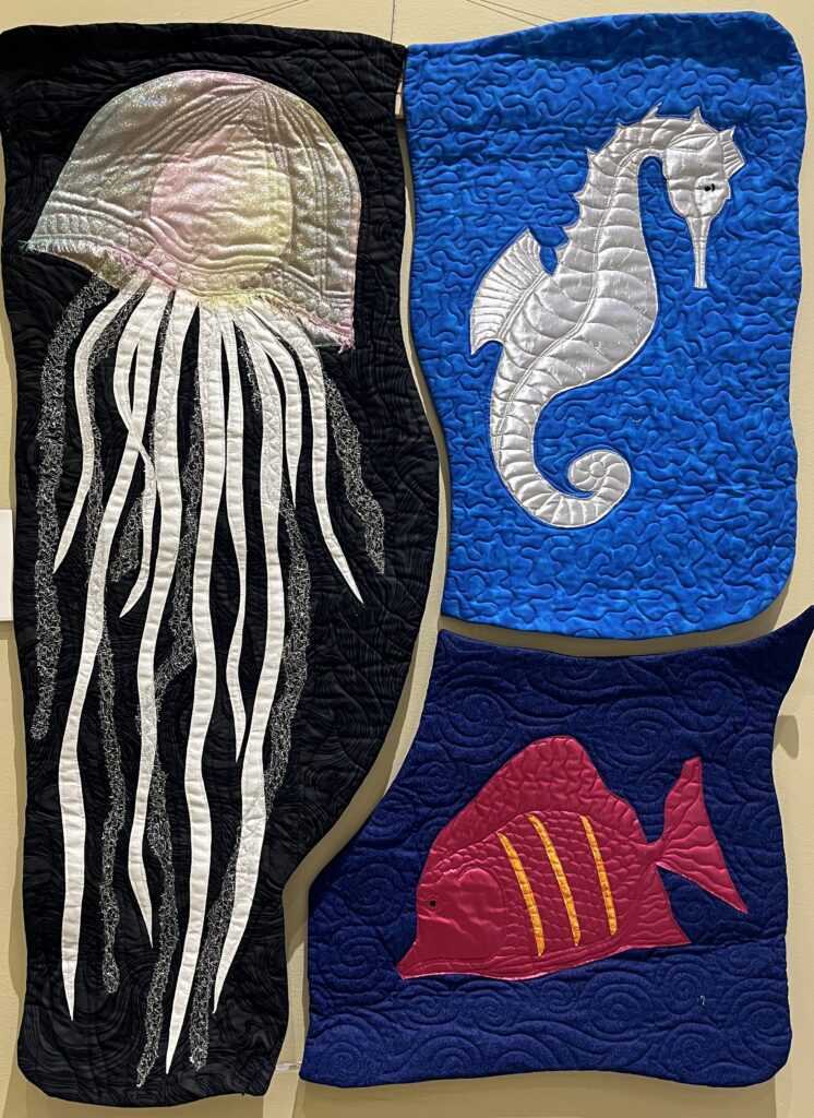 Three small quilts featuring a jellyfish, a seahorse, and a fish