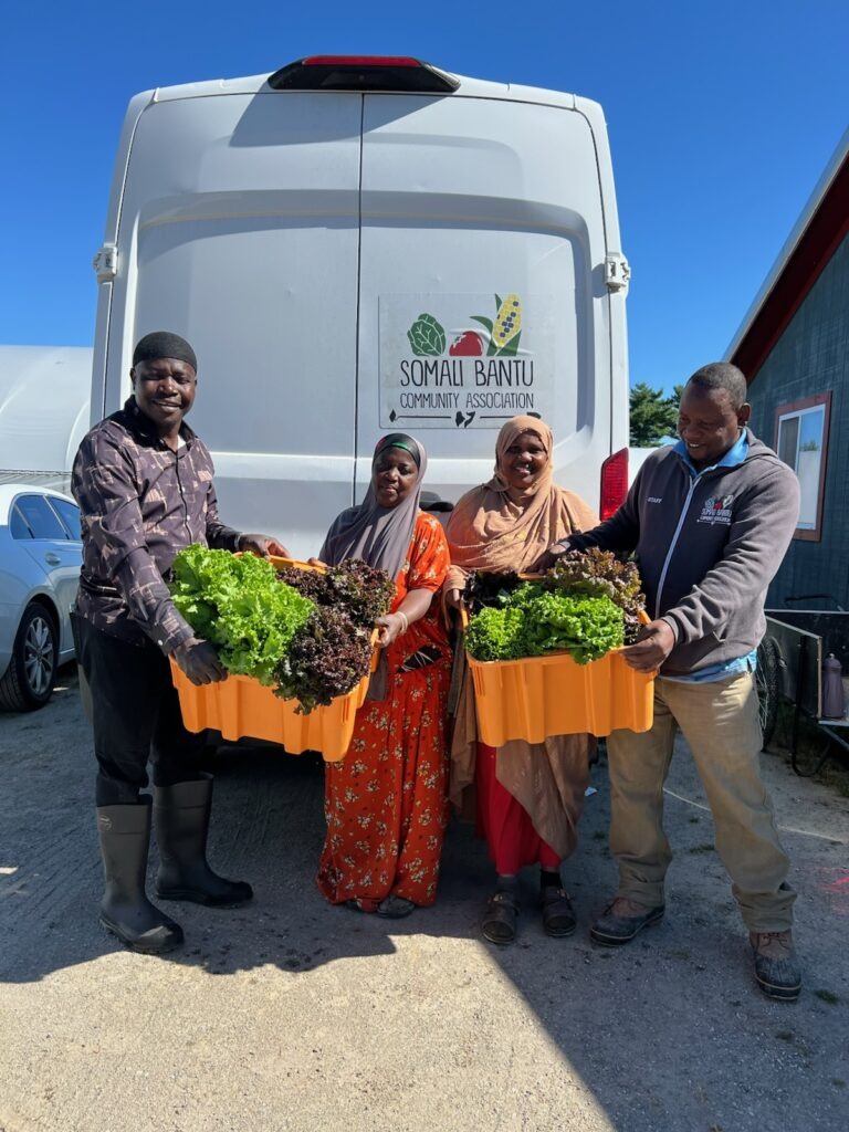 A group of people holding boxes of produce in front of a white van