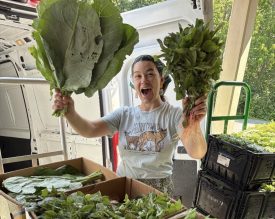 a woman holds up two heads of lettuce and smiles
